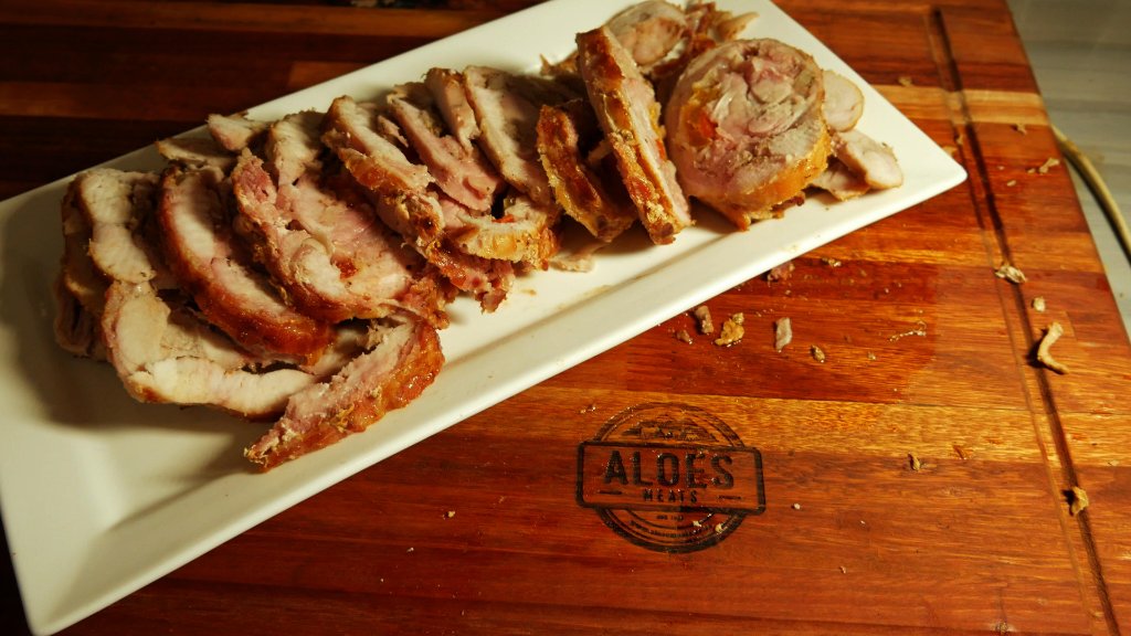 Sliced roasted pork carved and plated on a platter, resting on the Aloes Meats branded cutting board