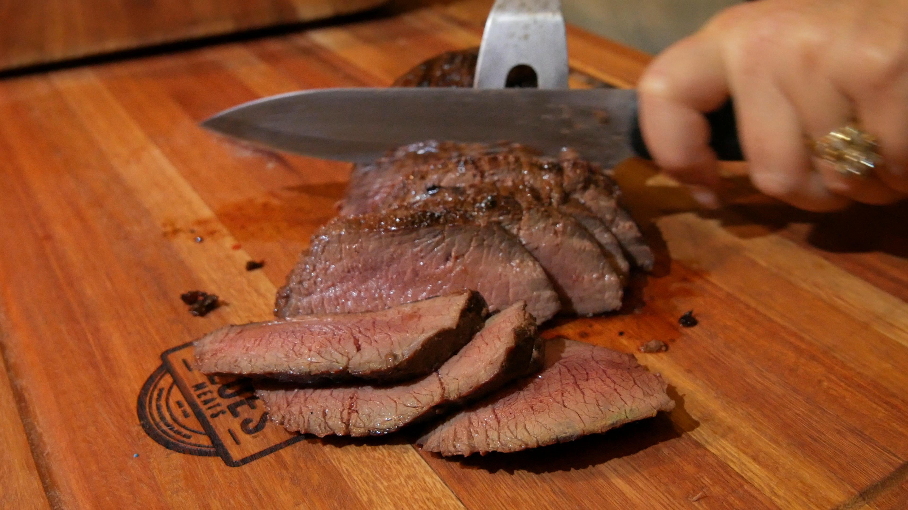 Aloes Meats sliced steak resting on a branded wooden cutting board, freshly carved with a knife
